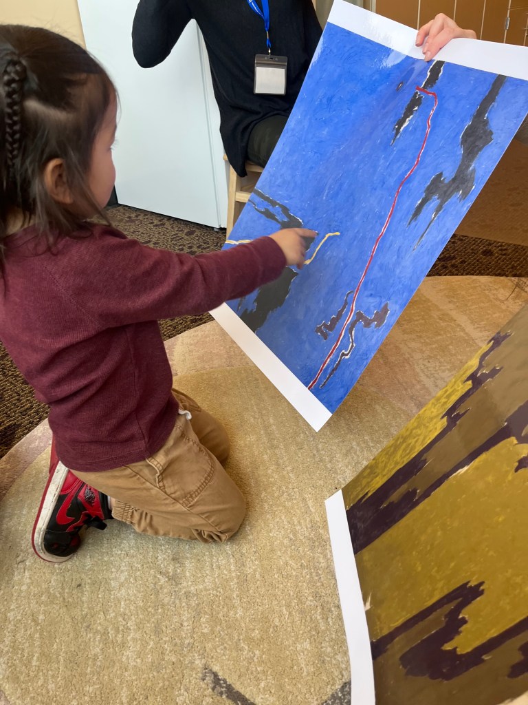 A young child kneeling, points to an image of an artwork.