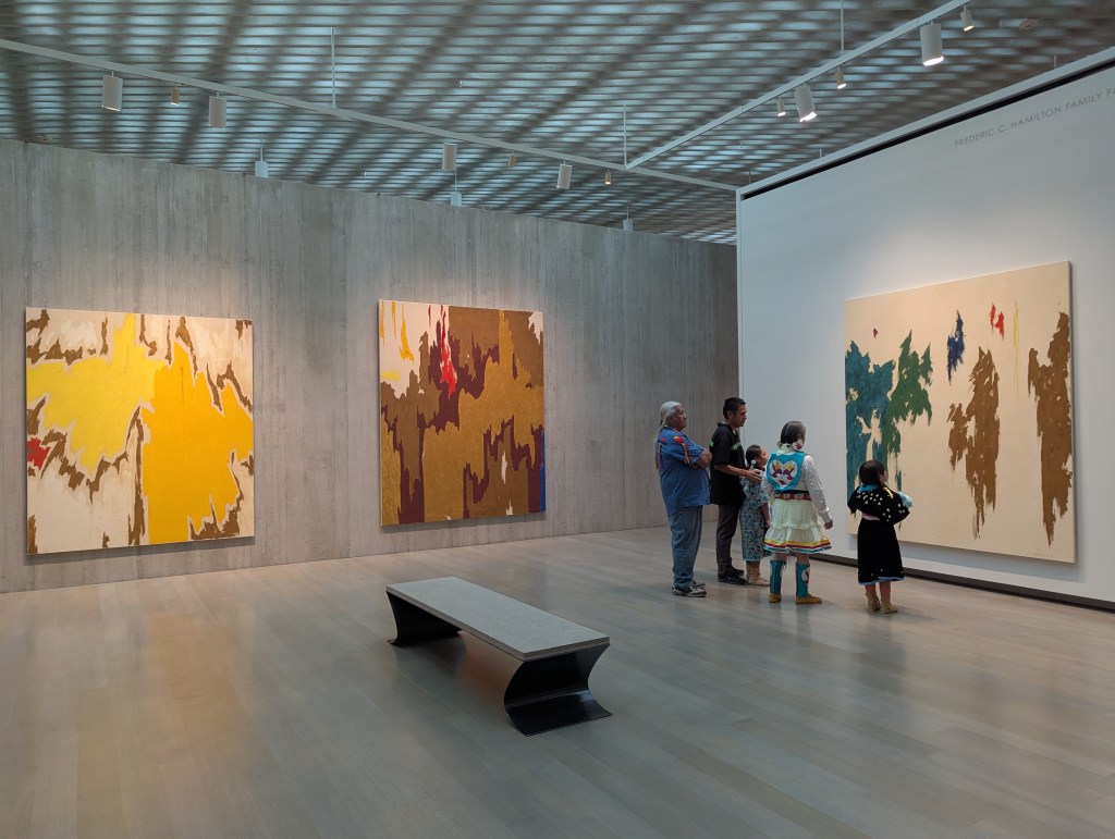 An image of a gallery with an intergenerational group of visitors viewing an artwork.