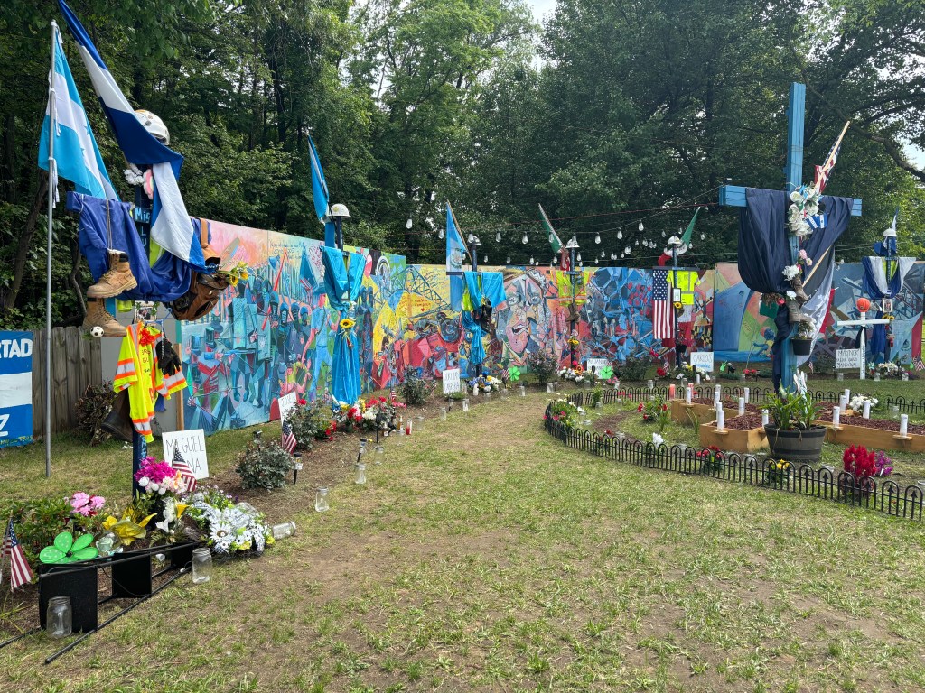 A colorful outdoor memorial with murals, crosses, flags, flowers, and tributes honoring the men who lost their lives in the Key Bridge collapse.