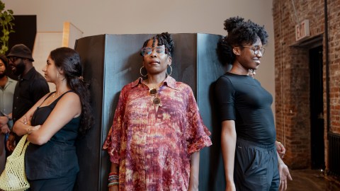 Three women stand with their backs to a hexagonal object experiencing stillness in different ways.