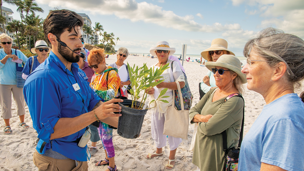 A man holding a potted plant out to a group of people on a beach.