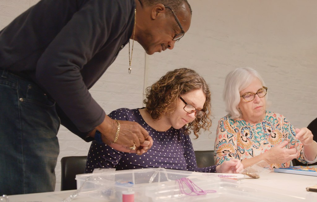 Two women and a male instructor taking a beading class.