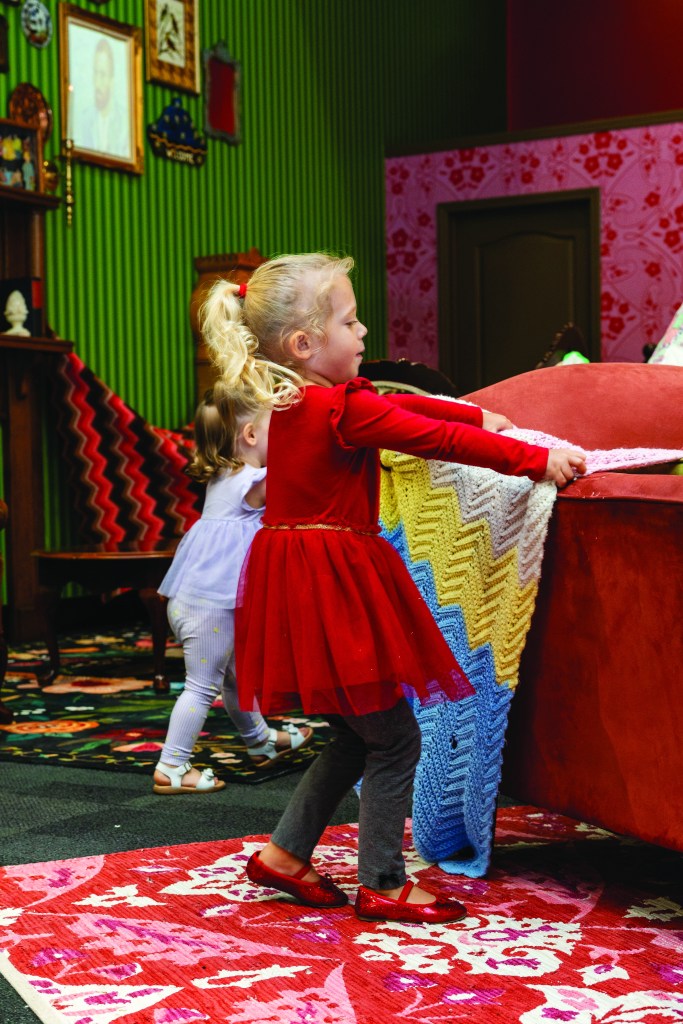 Two children are draping a blanket over a couch to make a fort.