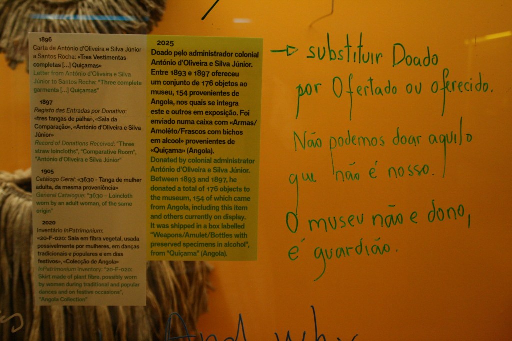 A close-up of the block labels printed in Portuguese and English against a warm yellow background. In Portuguese, green handwriting critiques the label’s text.