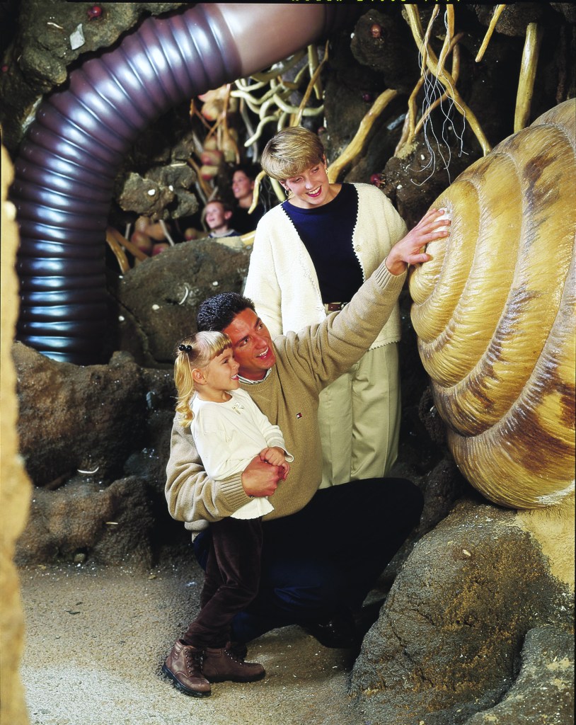 A couple and a child are looking at a giant snail shell model