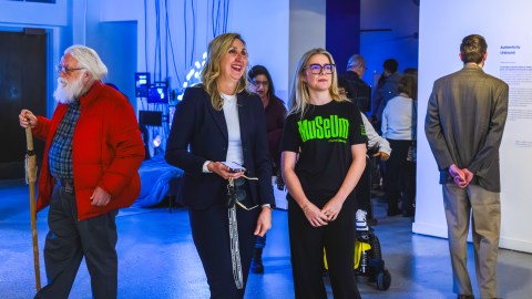 Visitors walk through a gallery during an opening reception, with one attendee engaging in conversation with a Museum CoLaborator while viewing the installation Dark Loops in the Blurred Realities exhibition.