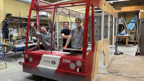 3 people inside a model of a bus cab inside a workshop.