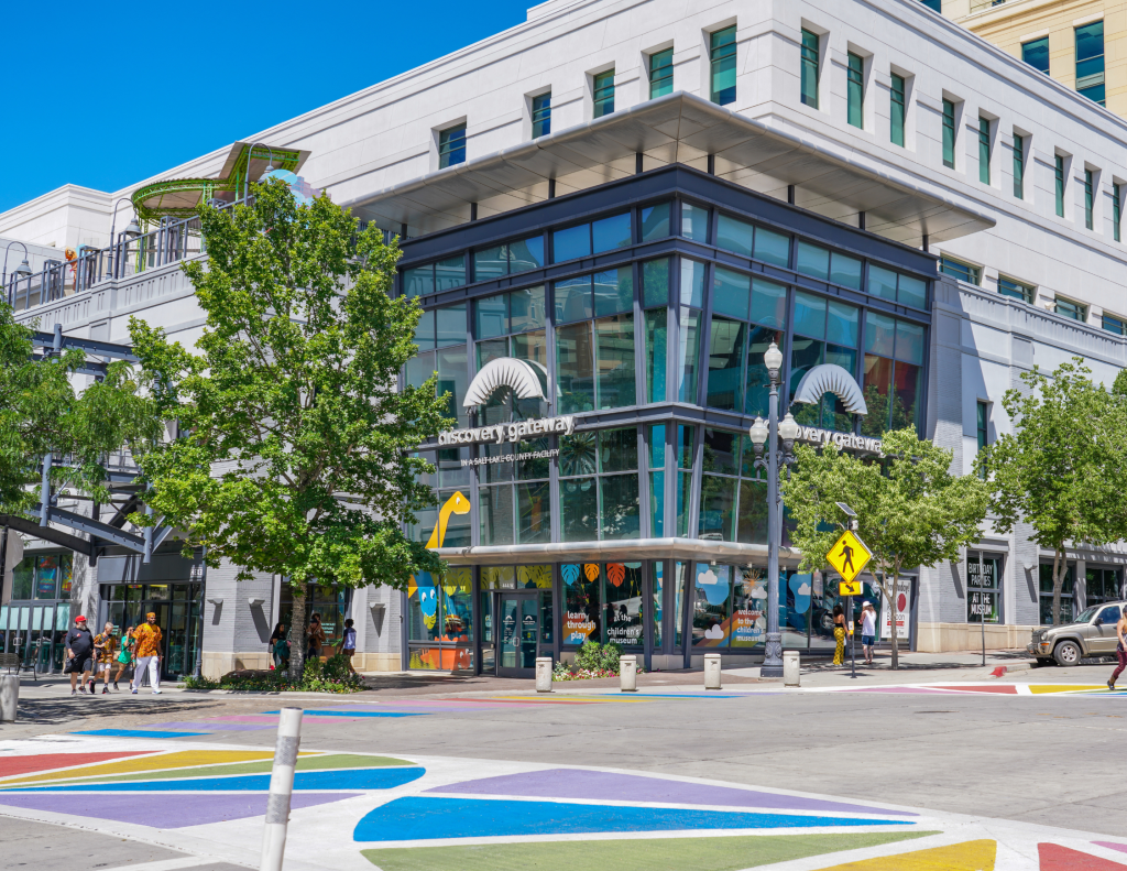 Exterior view of the Discovery Gateway Children's museum in Salt Lake City, a glass building on the corner of an intersection with colors painted on the street.