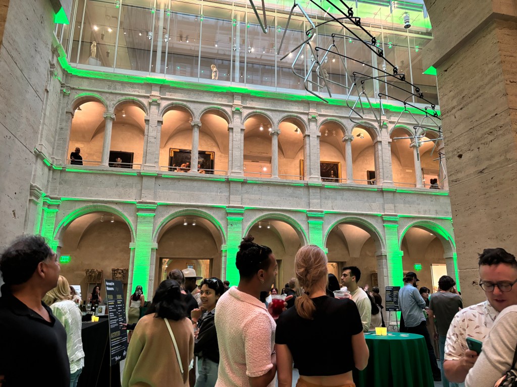 Visitors gathering in a large courtyard area with green lights and a mobile sculpture hanging overhead.