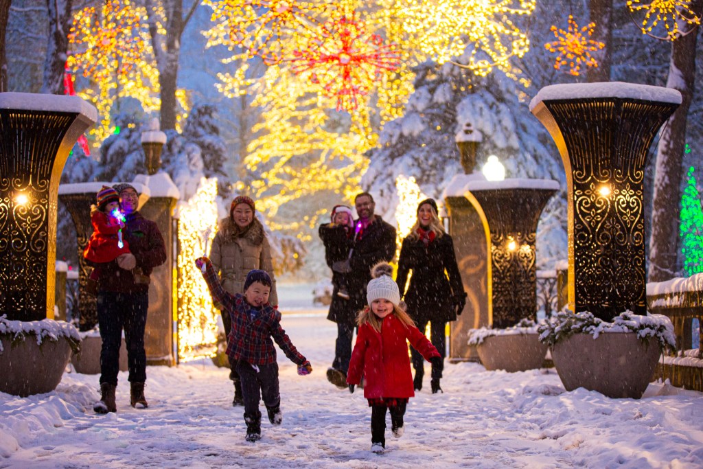 Adults and children walking through a snowy pathway with lighted decorative pedestals