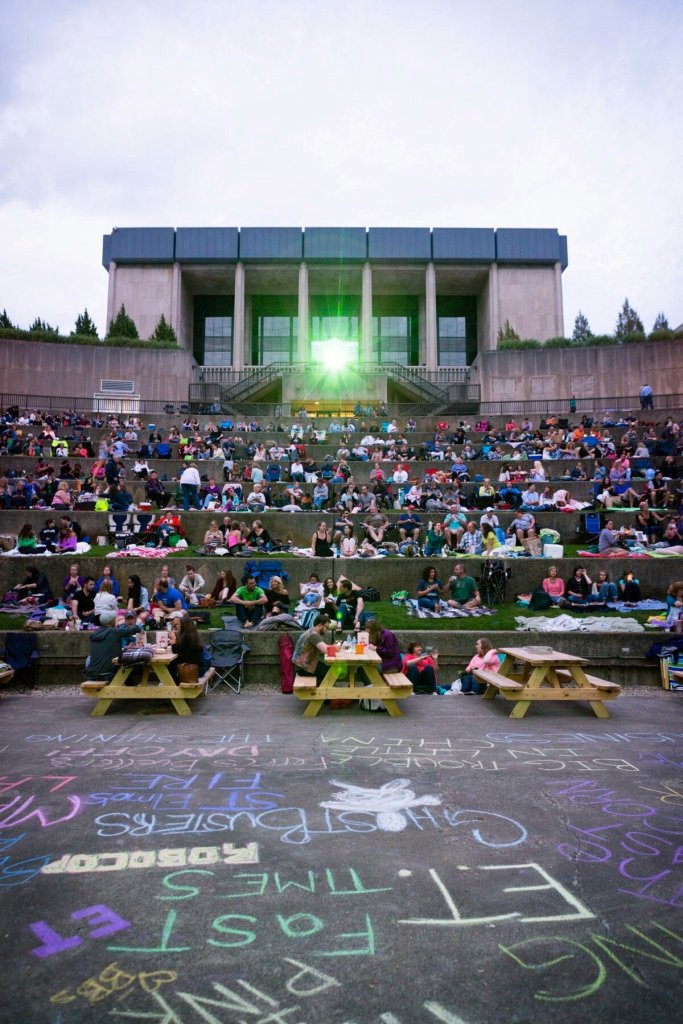 A crowd of people sitting in an outdoor amphitheater in front of a museum building