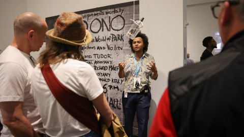 A museum docent is talking to a group of people in front of an artwork displayed on a wall.