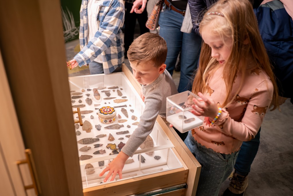 Two children standing in front of an open drawer with archaeological specimens in it.