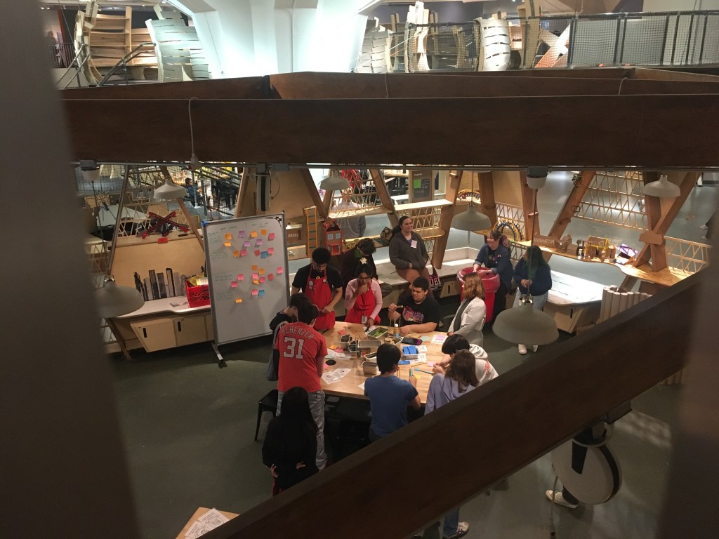 A group of adults doing an activity around a table in the middle of a room with sticky notes on a white board behind them.