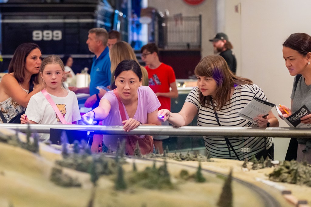 A group of people shine black lights into a small scale landscape model inside a museum.