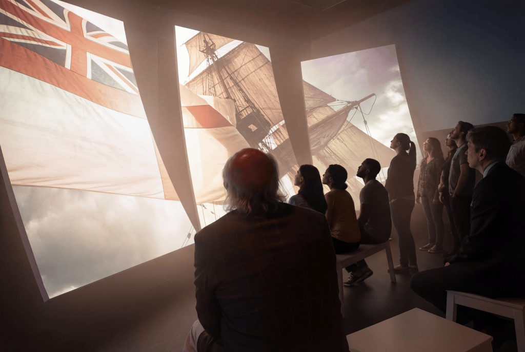 People watching a ship in a video projected onto a wall in a museum.