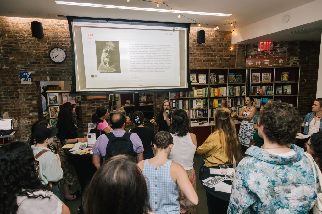 A person speaking to a group of people in a bookstore, with a projector screen displaying a vintage wedding photo and text above the audience.
