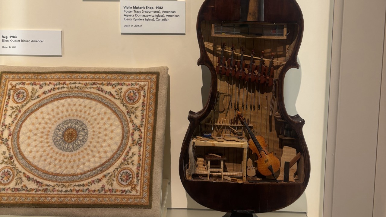 A finely detailed miniature violin maker’s shop invites close looking through tiny tools, furnishings, and workshop details arranged at a reduced scale.