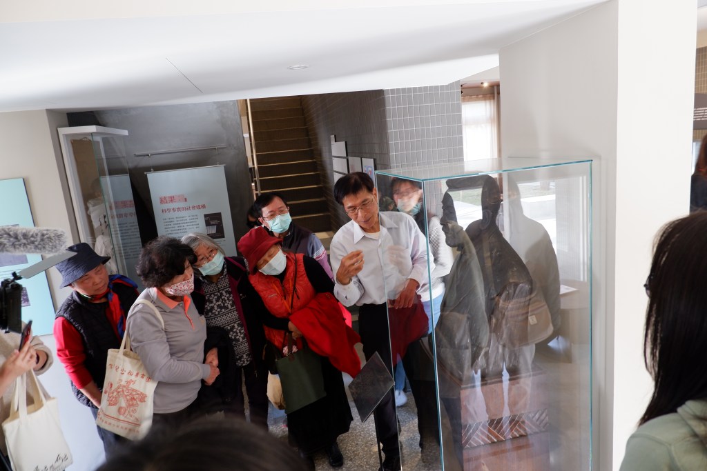 Audience members attend a public program in the exhibition space, with a speaker discussing Takagi Tomoe and public health history in front of his bust.