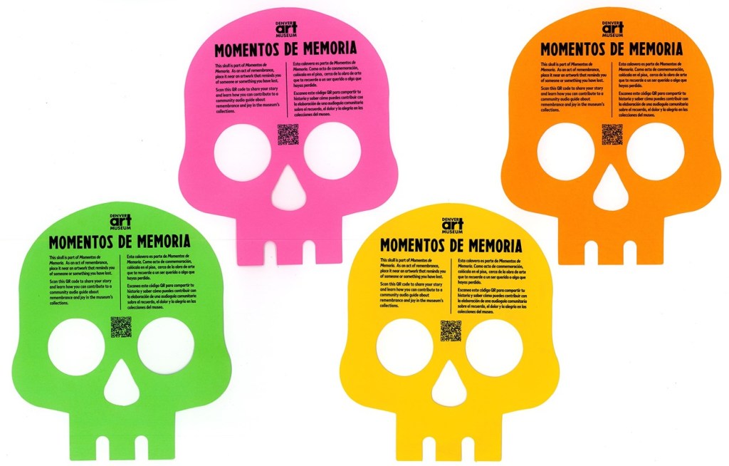 Four neon-colored, two-dimensional paper skulls. From left to right the colors are green, pink, yellow, and orange. Each card has the Denver Art Museum logo and the title "Momentos de Memoria" in bold black text, followed by bilingual instructions in English and Spanish and a QR code.