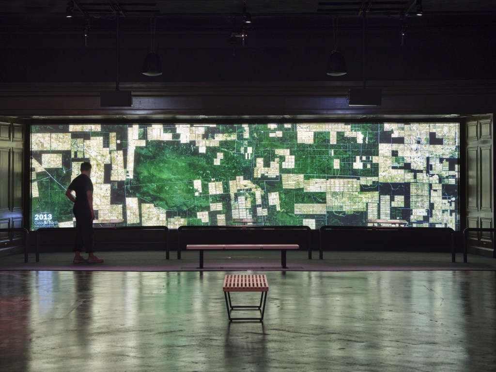 A visitor views a gigantic panorama showing satellite images of habitat loss. 
